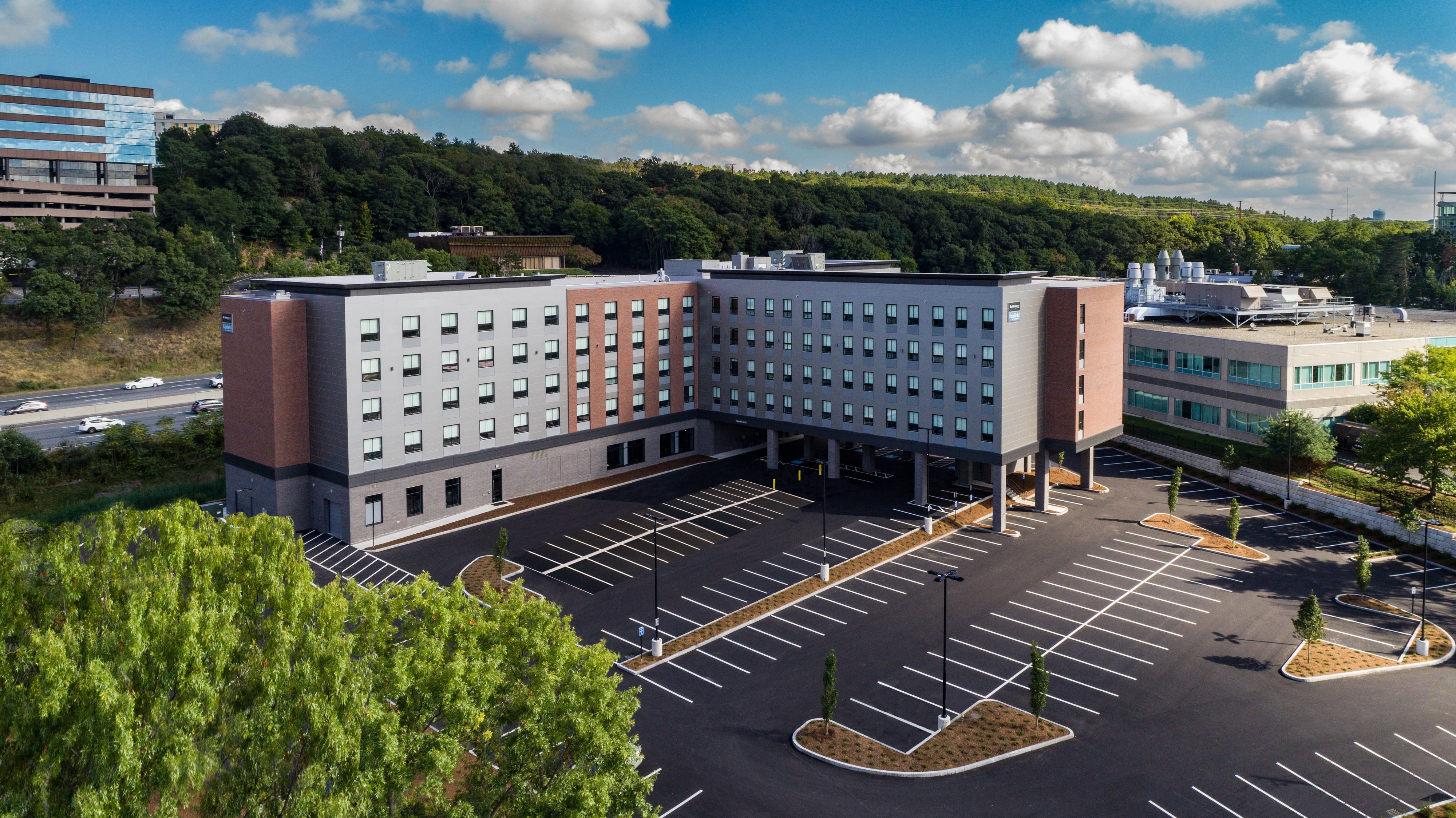 A multi-story hotel with a parking lot and a view of a forested hill in the background.
