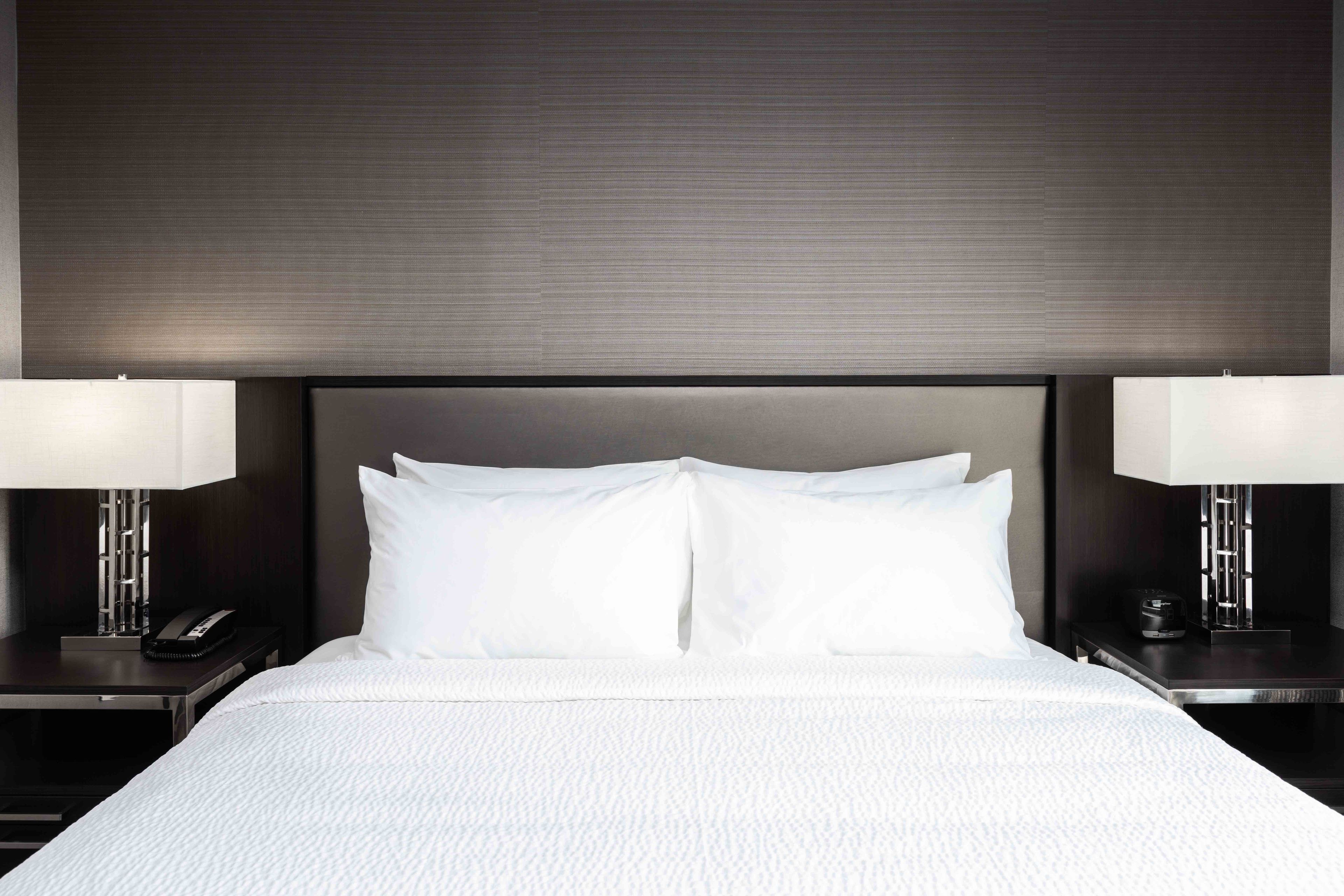 A neatly made bed with white linens, two bedside tables with lamps, and a dark headboard.