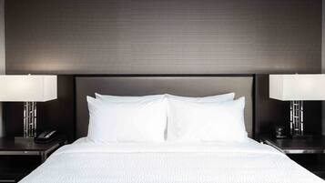 A neatly made bed with white linens, two bedside tables with lamps, and a dark headboard.