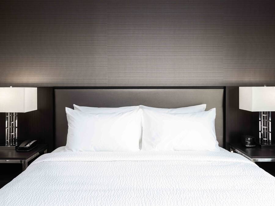 A neatly made bed with white linens, two bedside tables with lamps, and a dark headboard.