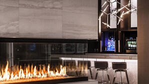 Un espace bar moderne doté d’une grande cheminée en verre transparent, de deux tabourets et d’un comptoir bien garni de bouteilles.
