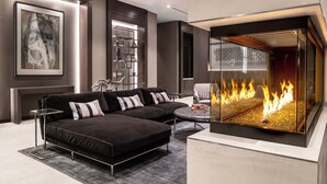 Un salon moderne avec un canapé d’angle, une table basse en verre et une cheminée où l’on peut voir les flammes.