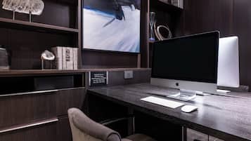 Un bureau moderne, équipé d’un ordinateur de bureau, d’un clavier et d’une souris. Une chaise est placée devant le bureau, et une étagère contient divers objets, notamment des livres et des objets décoratifs.
