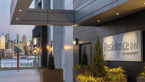 Une entrée d’hôtel moderne offrant une vue sur les gratte-ciel de la ville, de grands jardinières ornées de verdure et une enseigne indiquant « Residence Inn by Marriott ».