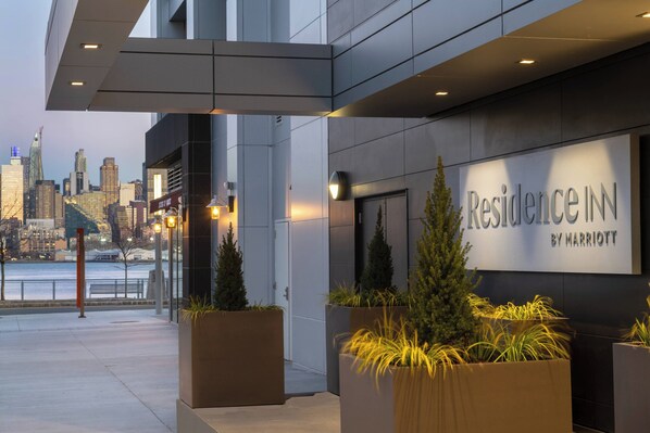 Una entrada moderna de hotel con vistas al horizonte de la ciudad, grandes macetas con plantas y un letrero que dice 'Residence Inn by Marriott'.