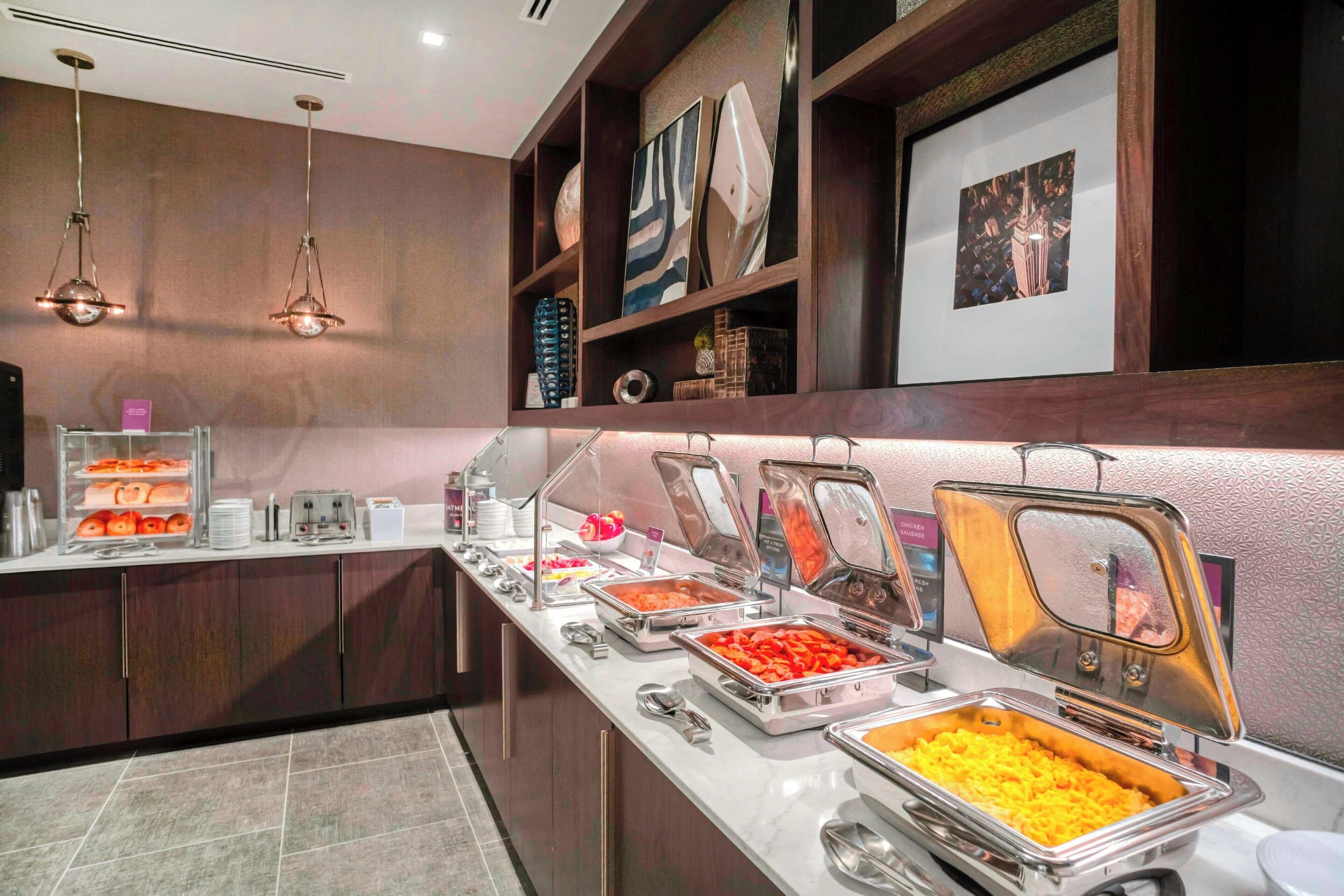 A buffet setup with various food items in metal containers, a counter with a glass display case, and decorative wall art.