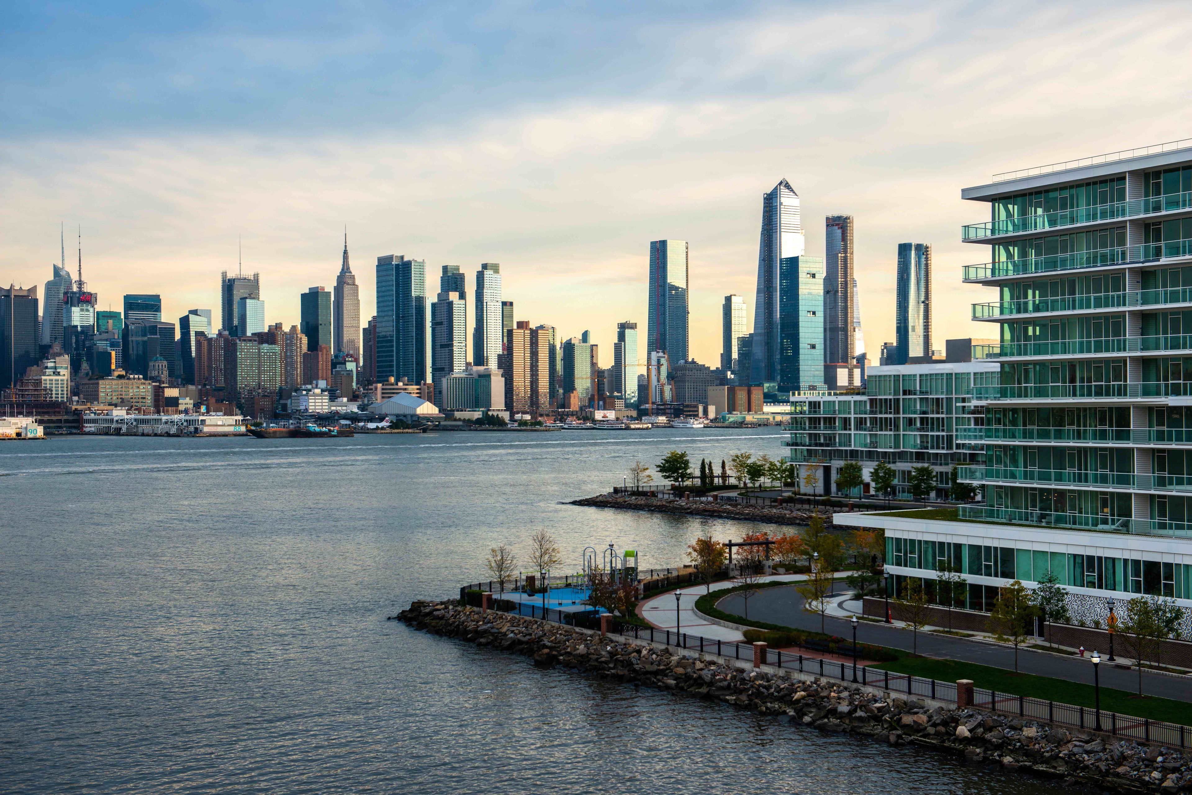 A waterfront cityscape with modern high-rise buildings, a marina, and a well-maintained promenade.