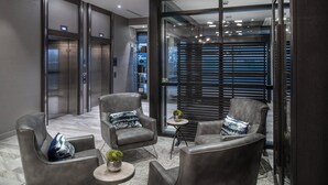 Un hall d’entrée moderne avec des fauteuils en cuir, une petite table ronde et une cloison en verre équipée de stores.