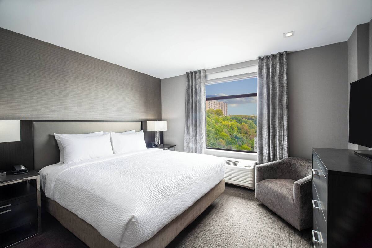 Een moderne hotelkamer met een groot bed, een bureau, een stoel, een televisie en een raam met uitzicht op de stad.