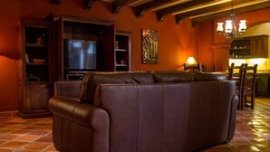 Un salon avec un canapé en cuir marron, un téléviseur et un coin repas comprenant des chaises et une table.
