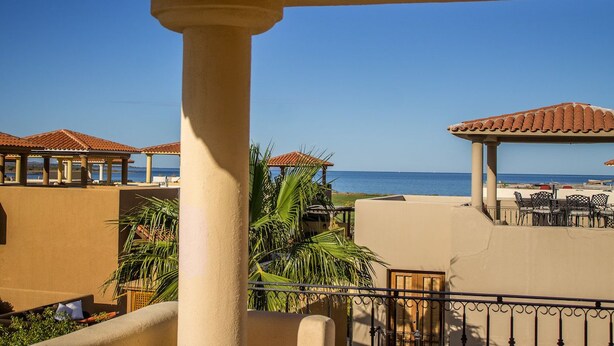 Un balcon avec vue sur la mer, des palmiers et des sièges d’extérieur.