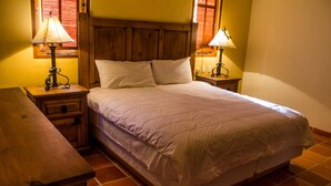 Une chambre à coucher avec une tête de lit en bois, deux tables de chevet avec des lampes, un lit avec une literie blanche et une table de nuit en bois.
