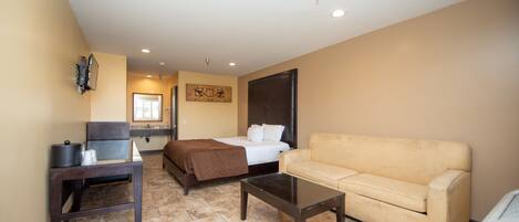 A hotel room with a bed, a sofa, a small table, a TV, and a kitchen area.