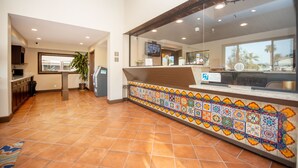 Una zona de recepción con suelo de baldosas, mostrador con borde de azulejos de colores, televisor y planta.