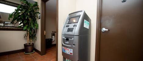 An ATM machine labeled "ATM Inside" in a hallway with tiled flooring, a potted plant, and a door with a sign indicating "Employee Only".