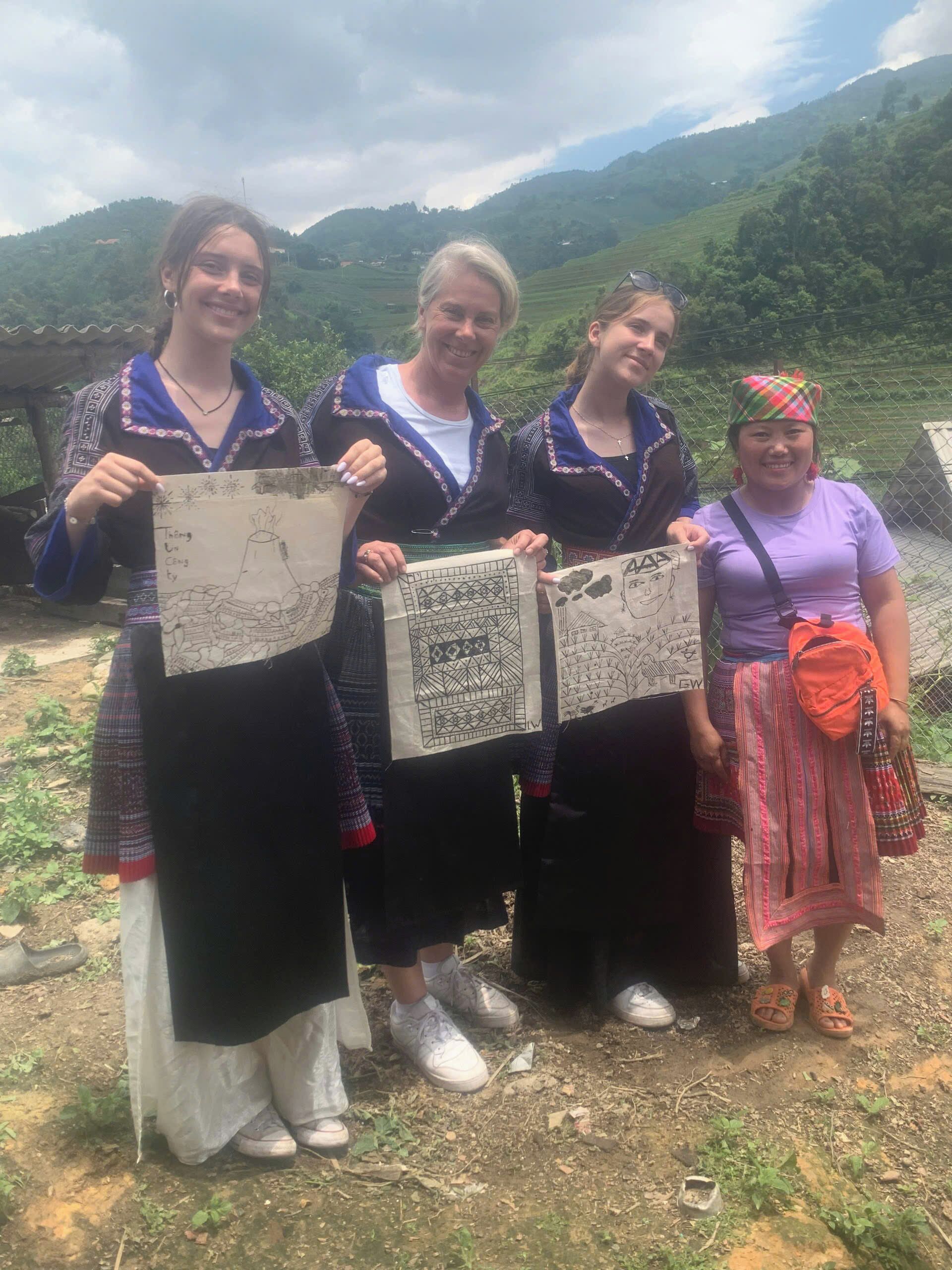 Three people holding handmade paper crafts outdoors with a mountainous backdrop.
