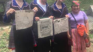 Three people holding handmade paper crafts outdoors with a mountainous backdrop.