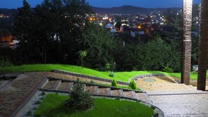 A landscaped garden with a patterned pathway, a small grassy area, and a view of a town at night. - FAVAR Carpathians (Skhidnytsia)