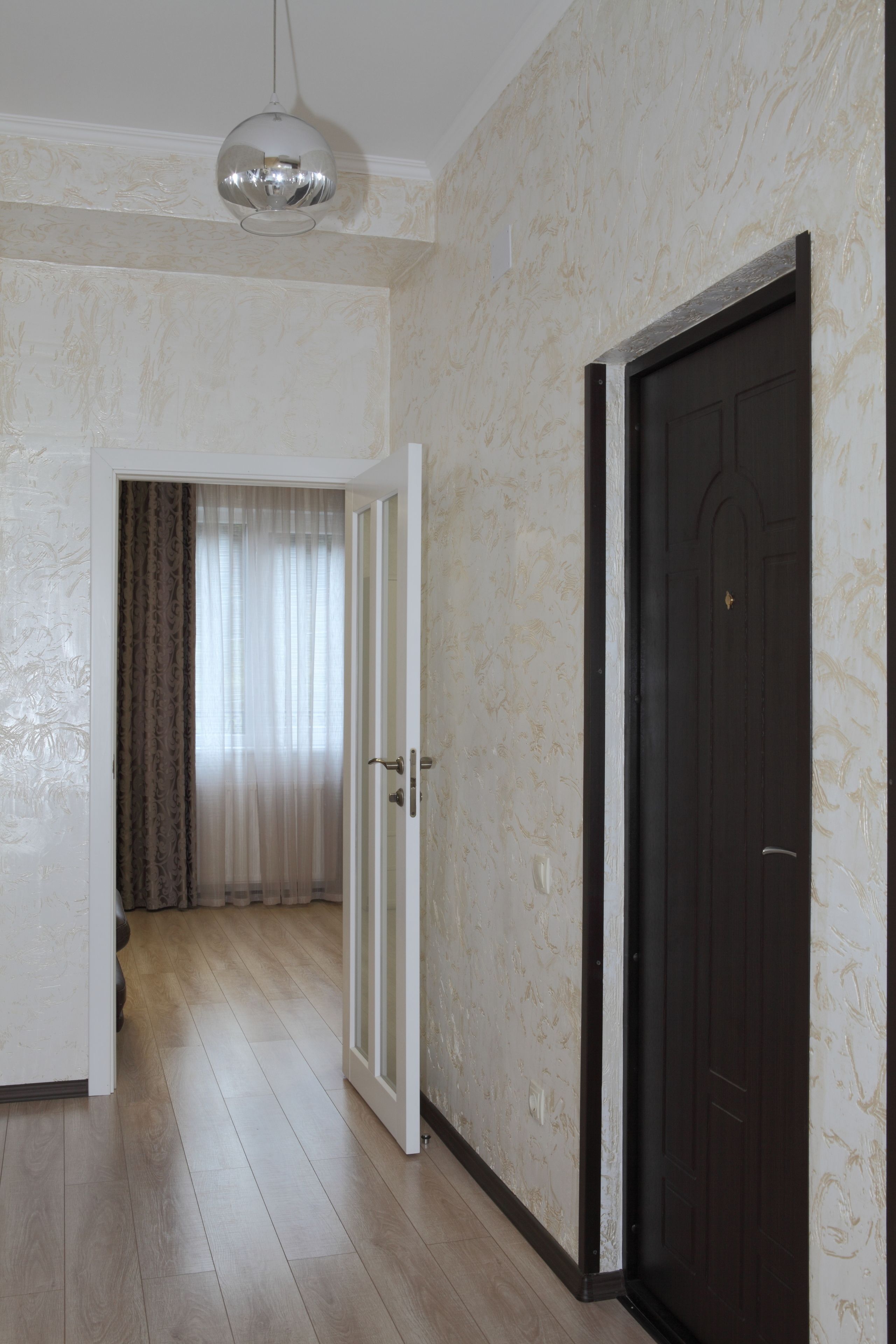 A hallway with a wooden floor, a dark door, and a light fixture.
