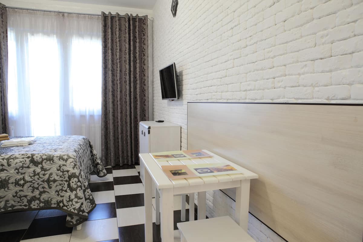 Quarto com uma cama, uma mesinha com fotos, uma televisão na parede e chão xadrez.