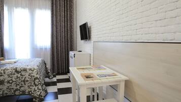 A room with a bed, a small table with photos, a TV on the wall, and a checkered floor.