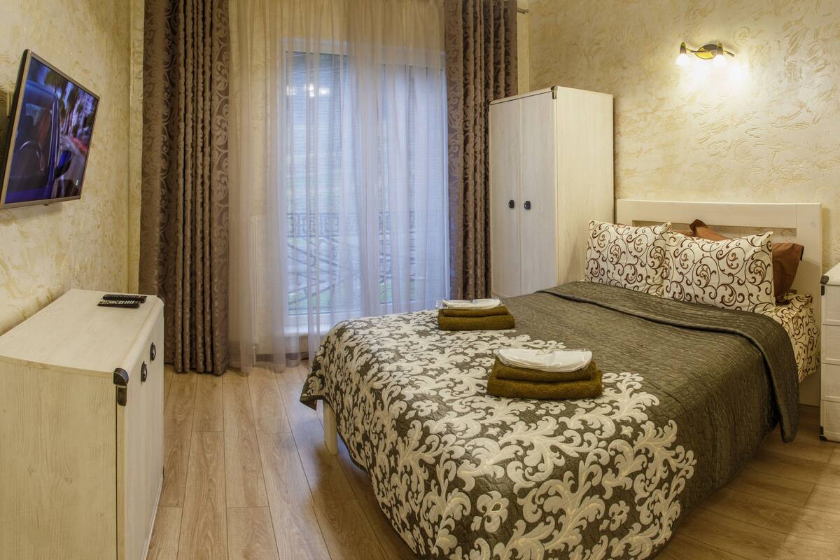 Quarto de hotel com uma cama, um guarda-roupa, uma televisão e uma escrivaninha.