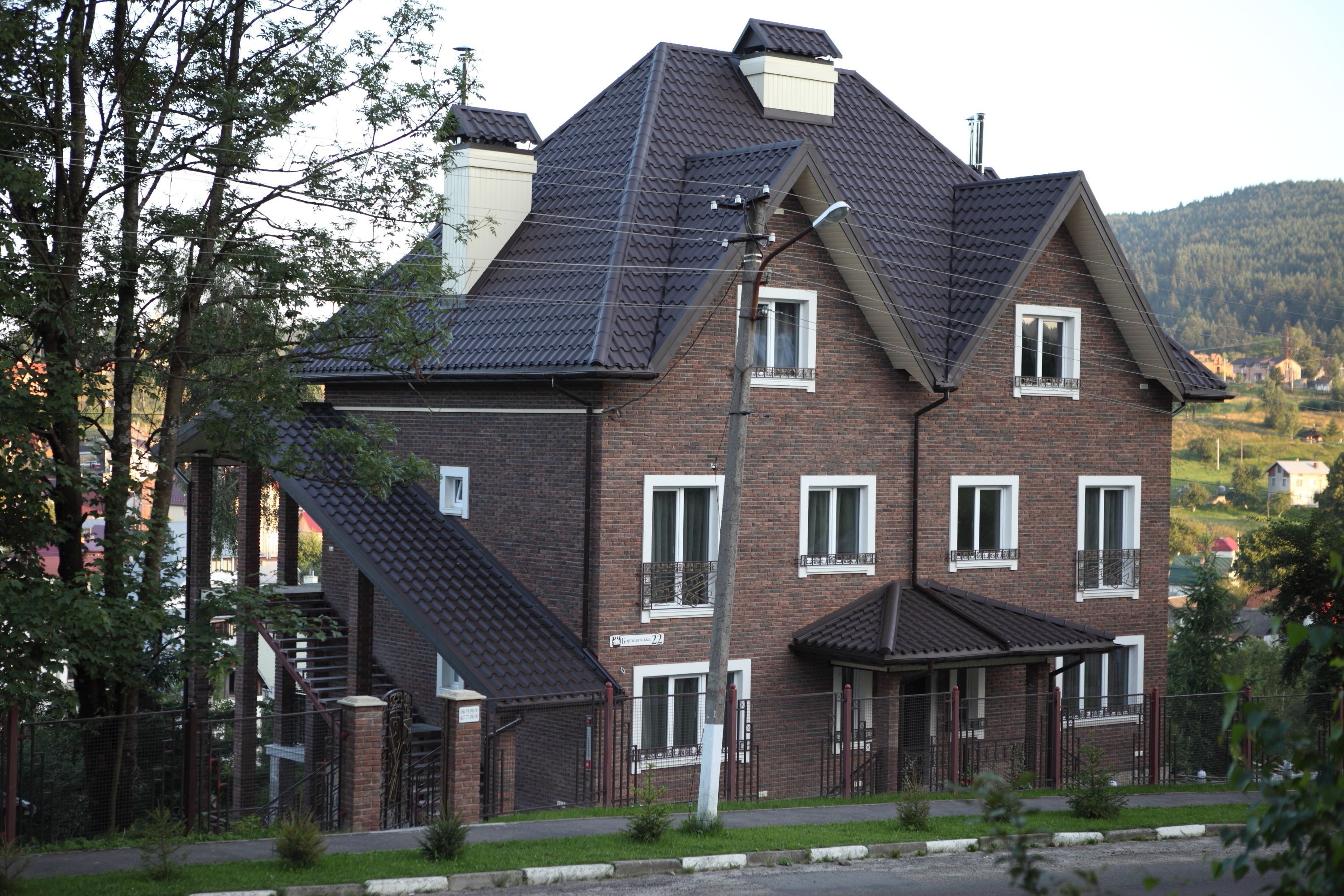 Una casa de ladrillo de dos pisos con un techo pronunciado, numerosas ventanas y una escalera visible que conduce a la entrada.