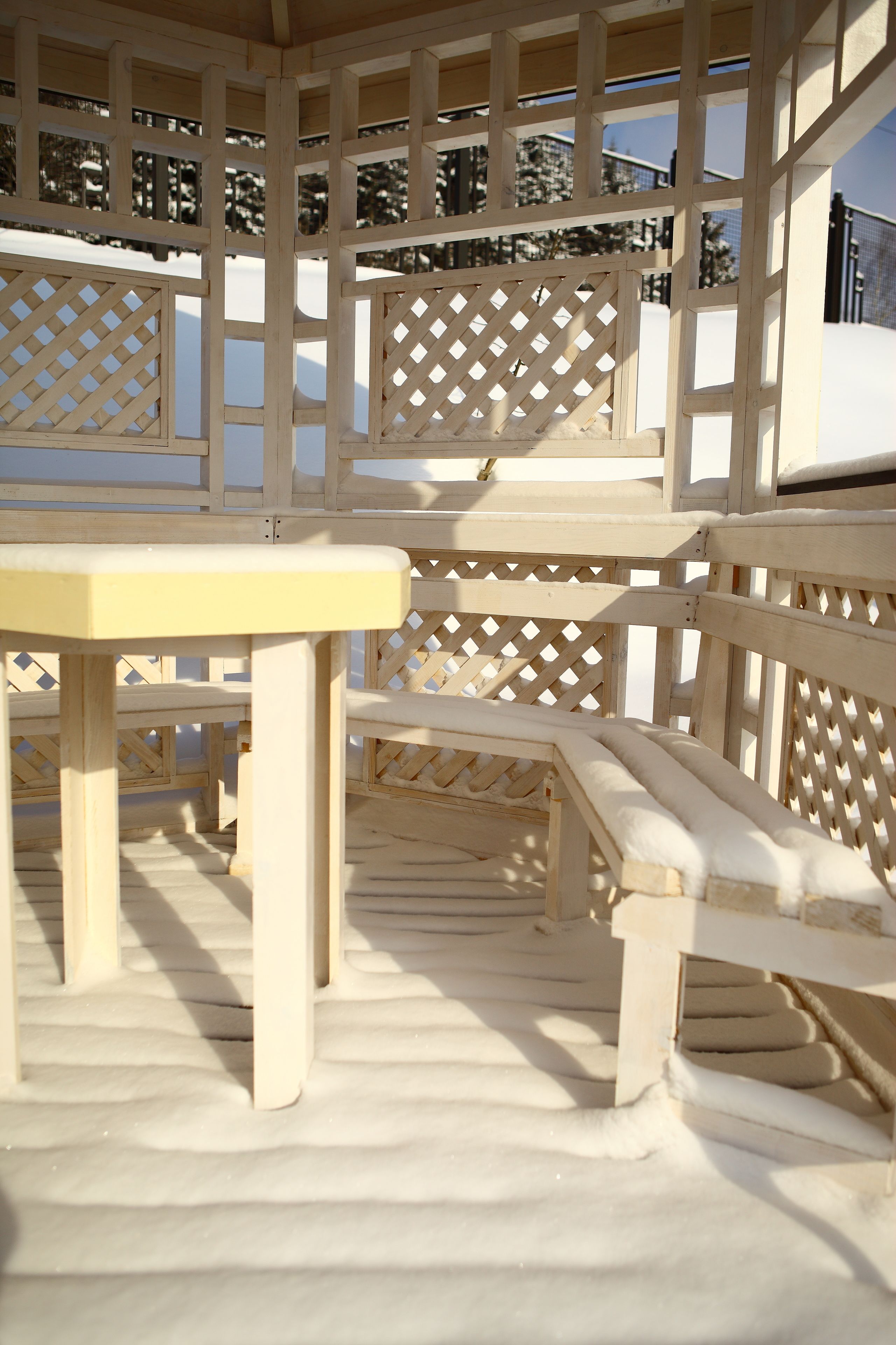 A wooden gazebo with a table and benches, surrounded by snow.