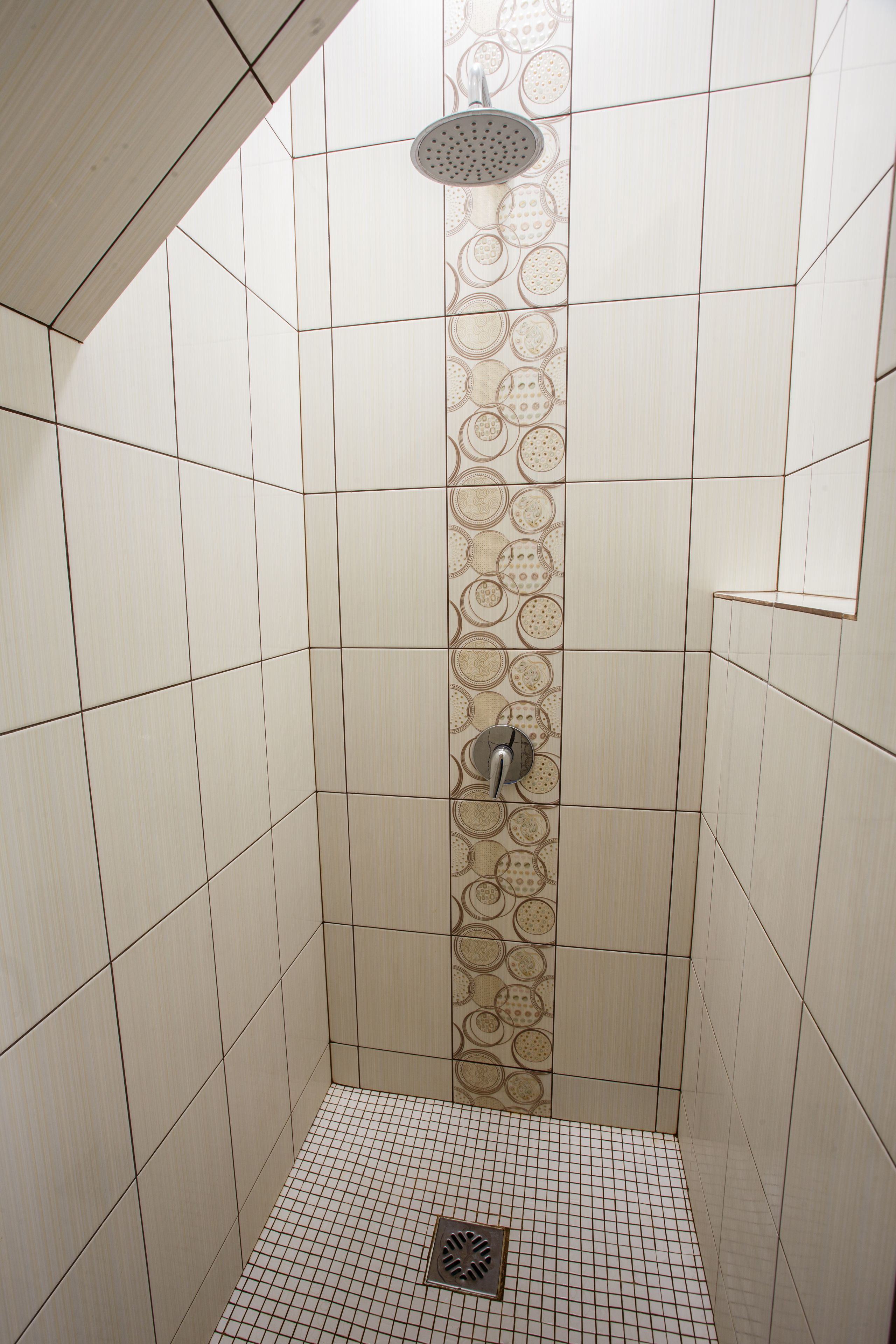 Een douche met een betegelde wand, een douchekop en een afvoer.