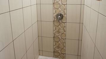 Een douche met een betegelde wand, een douchekop en een afvoer.