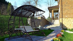 A garden with a metal swing chair, a stone wall, and a brick pathway leading to a building entrance. - FAVAR Carpathians (Skhidnytsia)