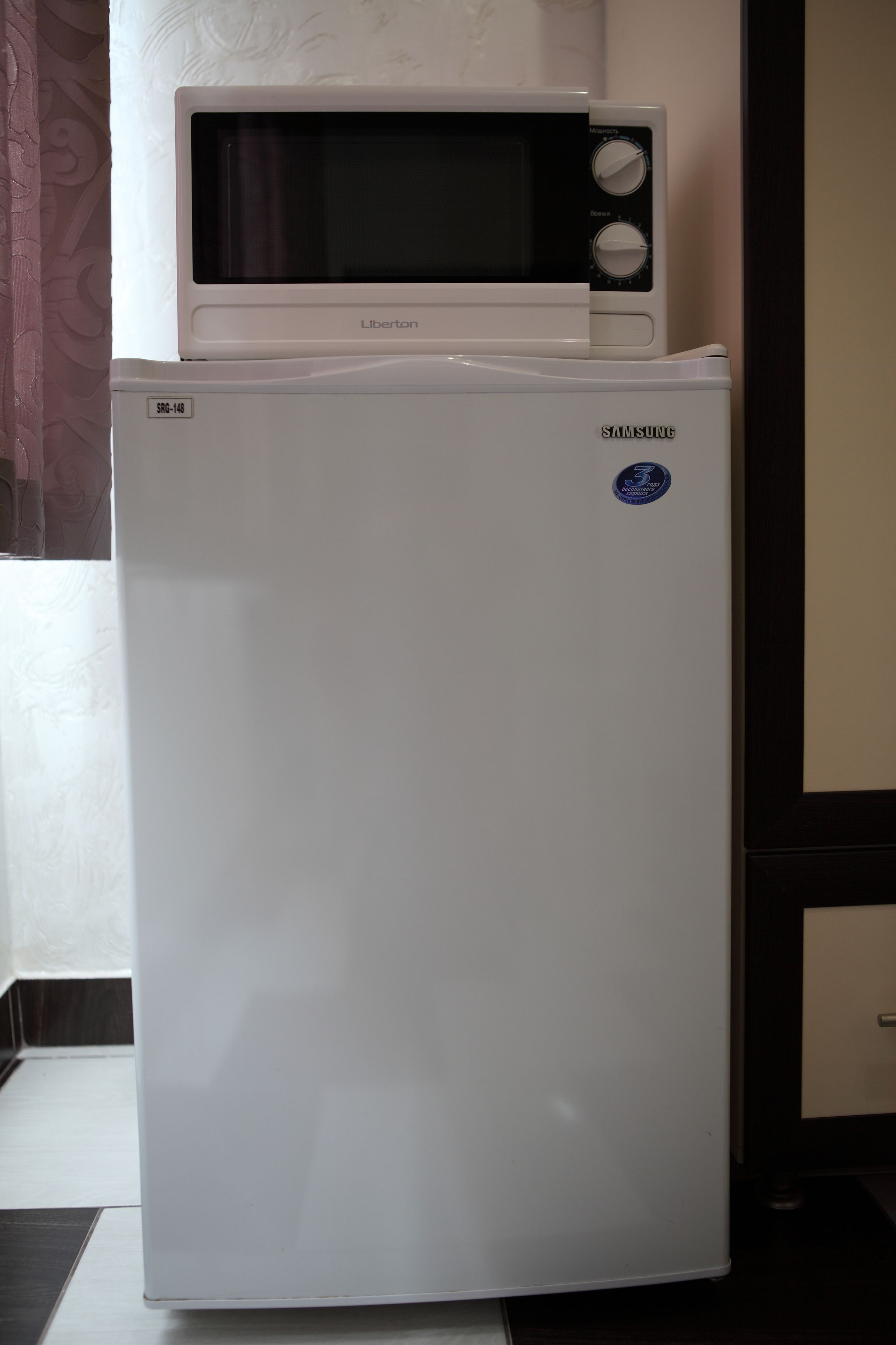 A white refrigerator with a microwave on top, a Samsung logo, and a sticker with the number 3.