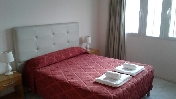 A neatly made bed with a red quilt and two white towels on the side.