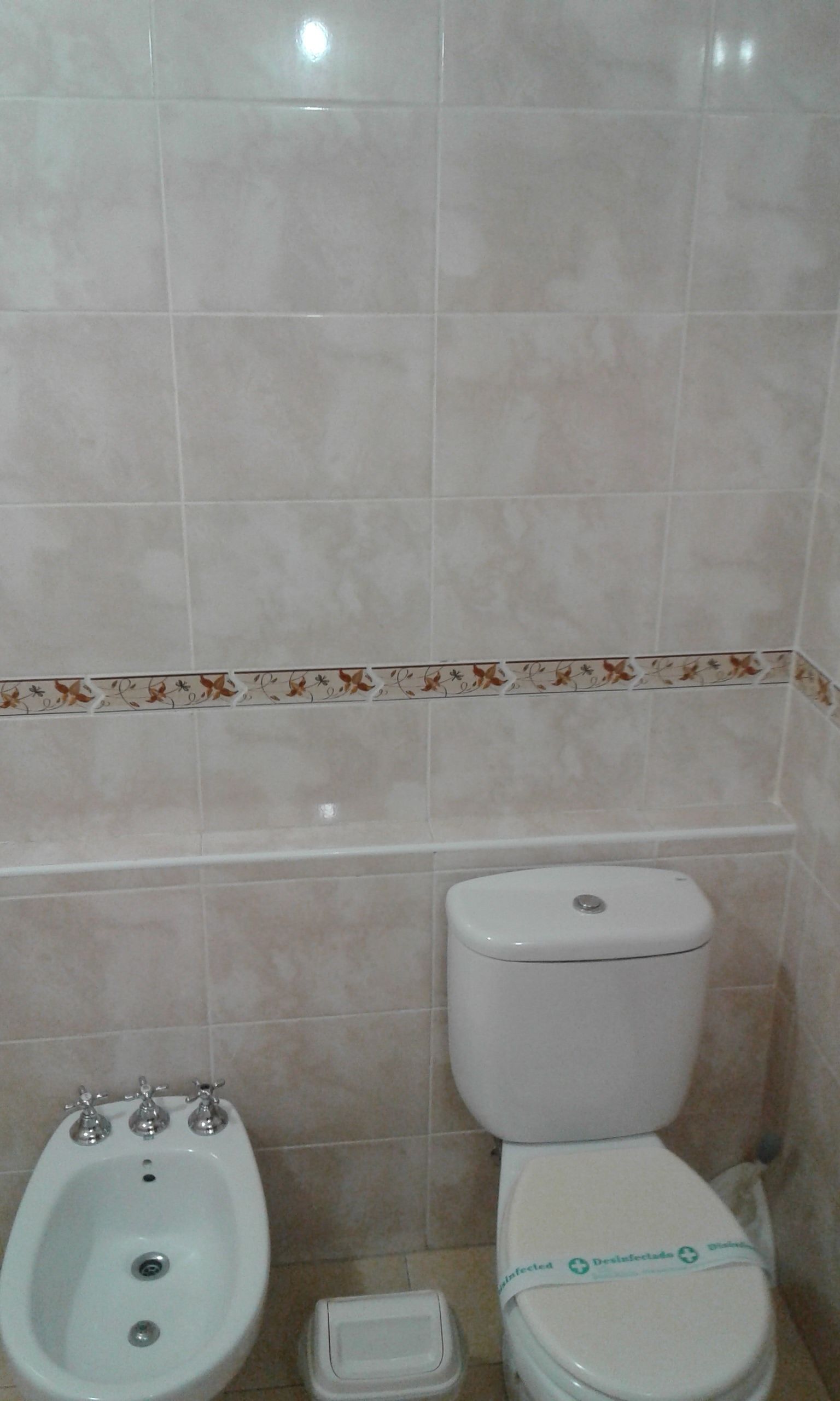 A bathroom with a bidet, toilet, and a small trash bin.