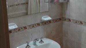 A bathroom with a sink, mirror, shower curtain, and a shelf with toiletries.