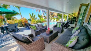 A covered outdoor seating area with wicker furniture, a pool, and tropical plants. - Natura Beach Pool Villa 2 (Rarotonga)