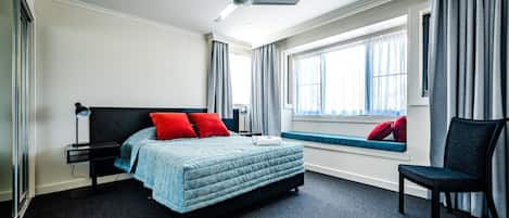 Ein modernes Hotelzimmer mit Bett, Schreibtisch, Stuhl, Deckenventilator und einem Vorhangfenster.