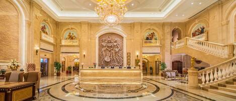 A grand lobby with a central reception desk, a large chandelier, and a grand staircase.