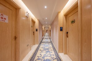 A hotel corridor with wooden doors, a patterned carpet, and signs indicating room numbers. - Vienna Hotel (Shenzhen)