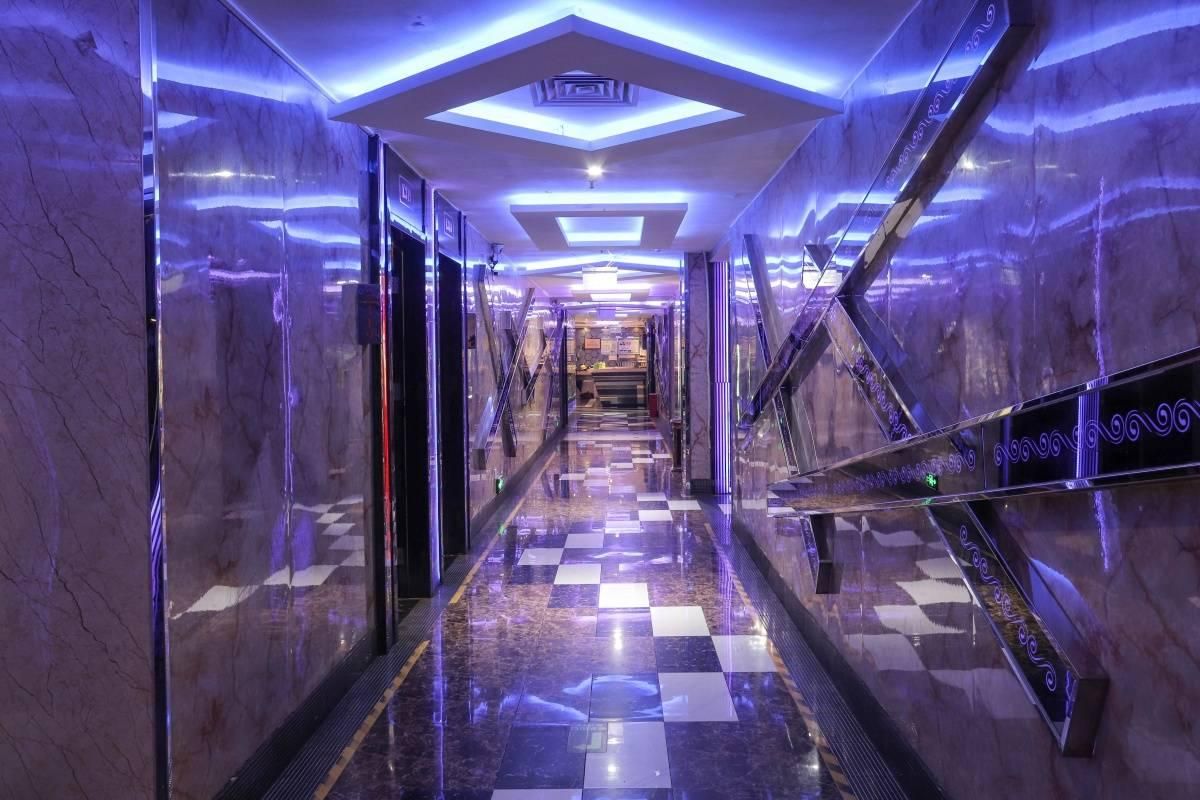 A corridor with a checkered floor, marble walls, and a ceiling with geometric lighting.