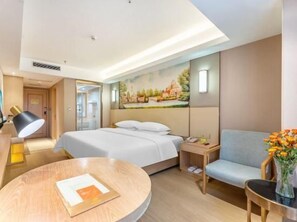 A hotel room with a bed, a desk, a chair, a round table, and a painting on the wall.