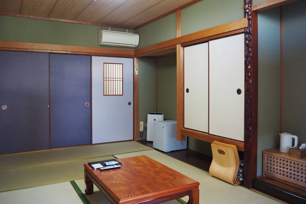 A traditional Japanese room with tatami flooring, a wooden table, sliding doors, and a ceiling fan.