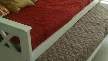 A single-bed room with a white frame, red bedding, and a brown quilted mattress.