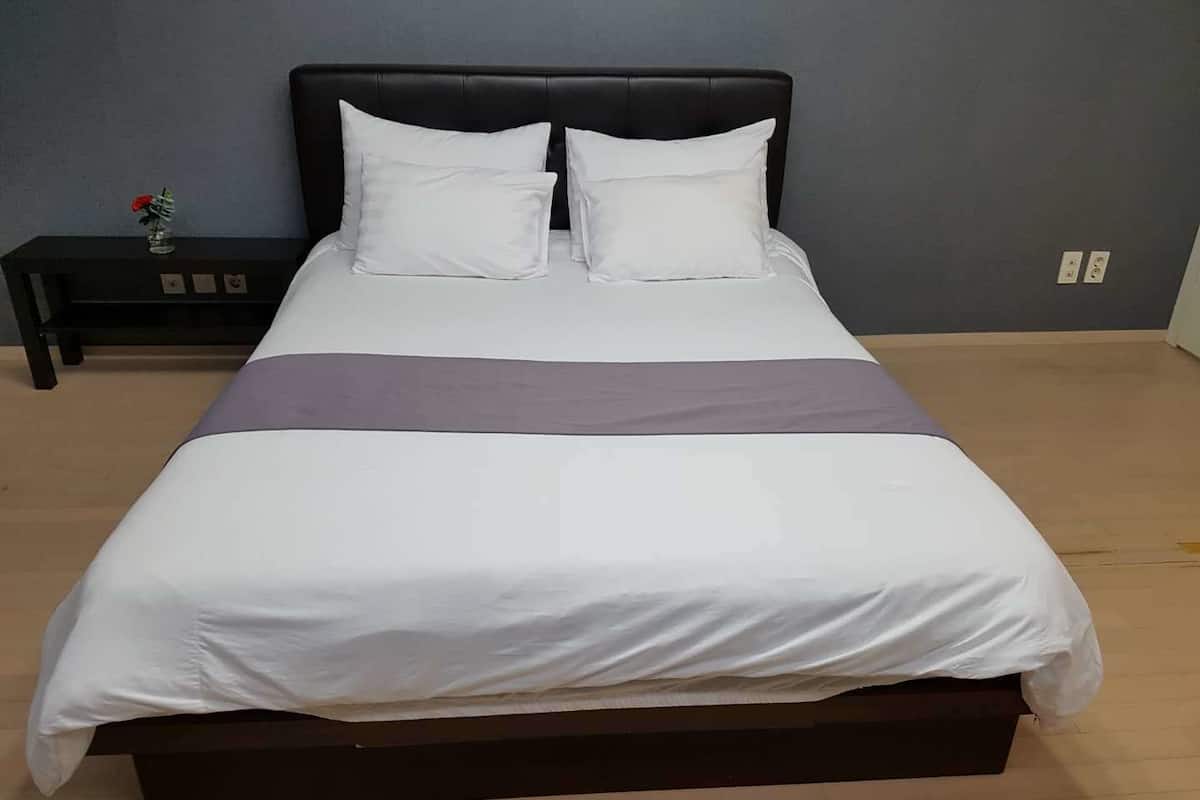 A bed with a dark headboard, white bedding, and a purple accent.