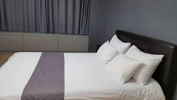 A neatly made bed with white and gray linens and two pillows, a gray accent pillow, and a dark headboard in a room with gray walls and a window with curtains.
