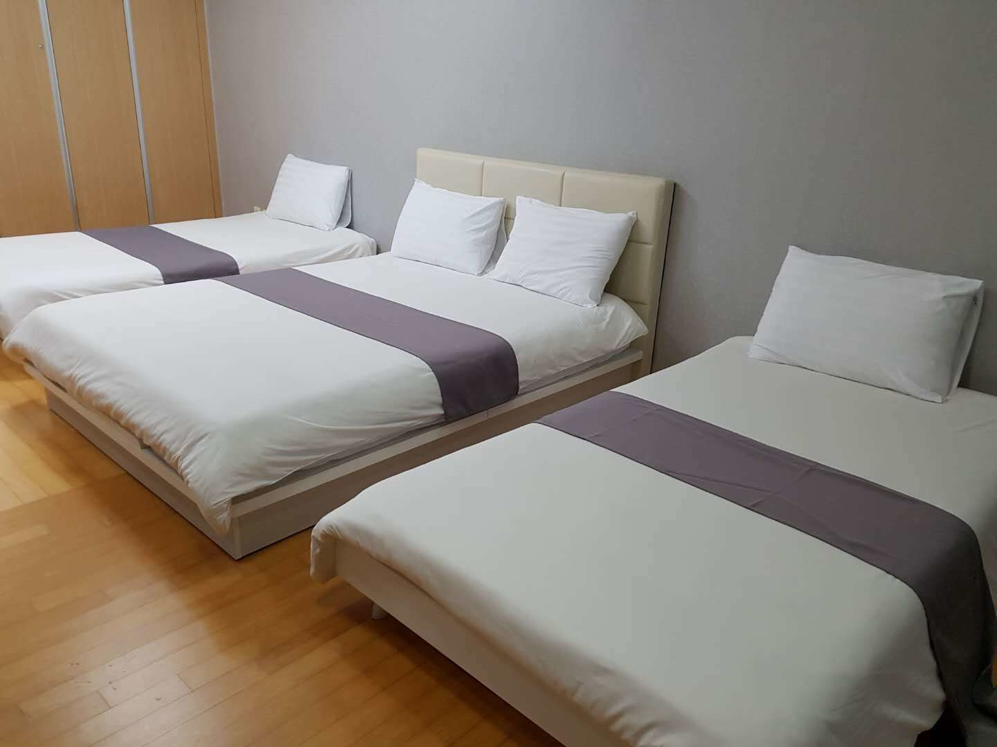 A hotel room with three beds arranged in a row, each with white bedding and a grey accent.