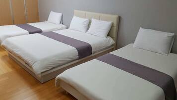 A hotel room with three beds arranged in a row, each with white bedding and a grey accent.