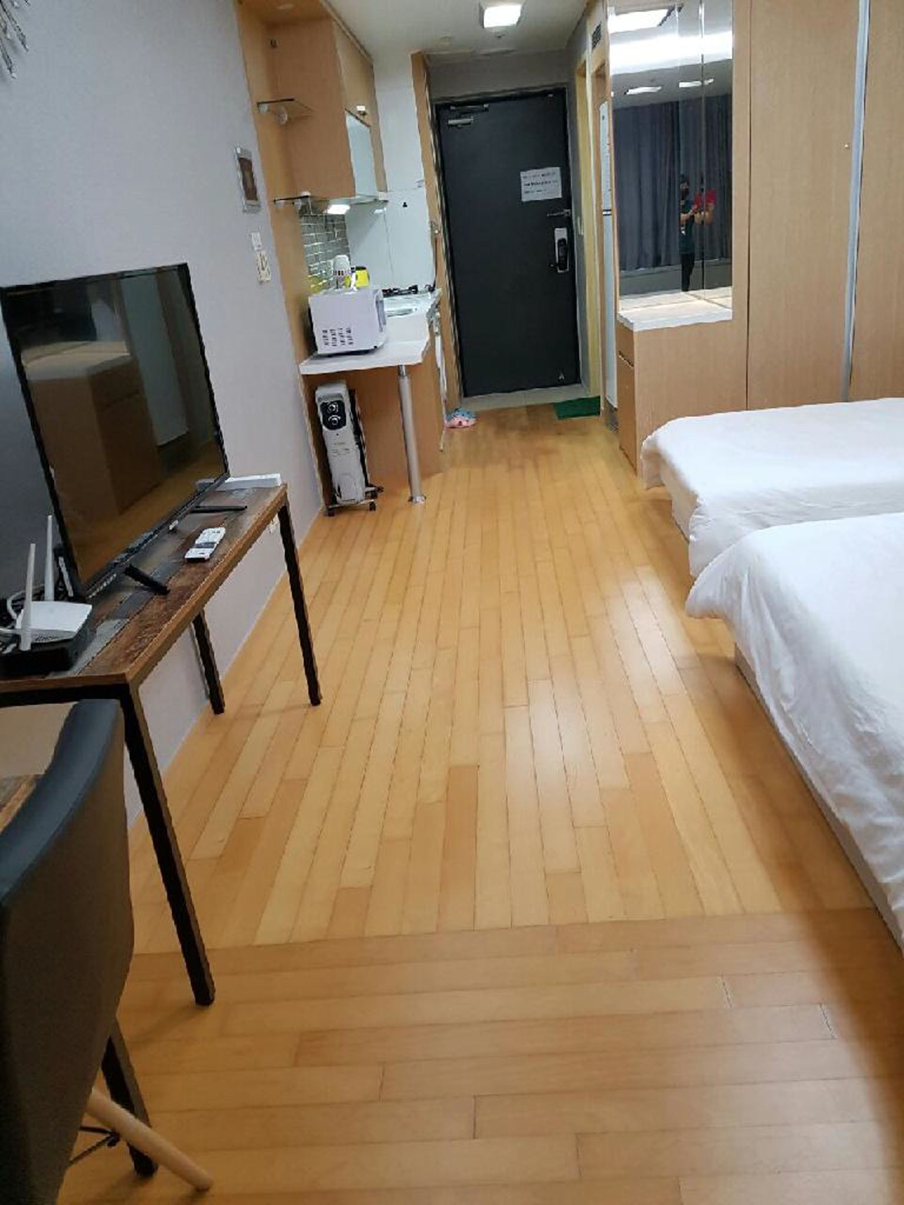 Una camera d'albergo con pavimento in legno, un letto, una scrivania con un computer, una televisione e uno specchio.