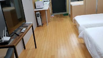 Una camera d'albergo con pavimento in legno, un letto, una scrivania con un computer, una televisione e uno specchio.