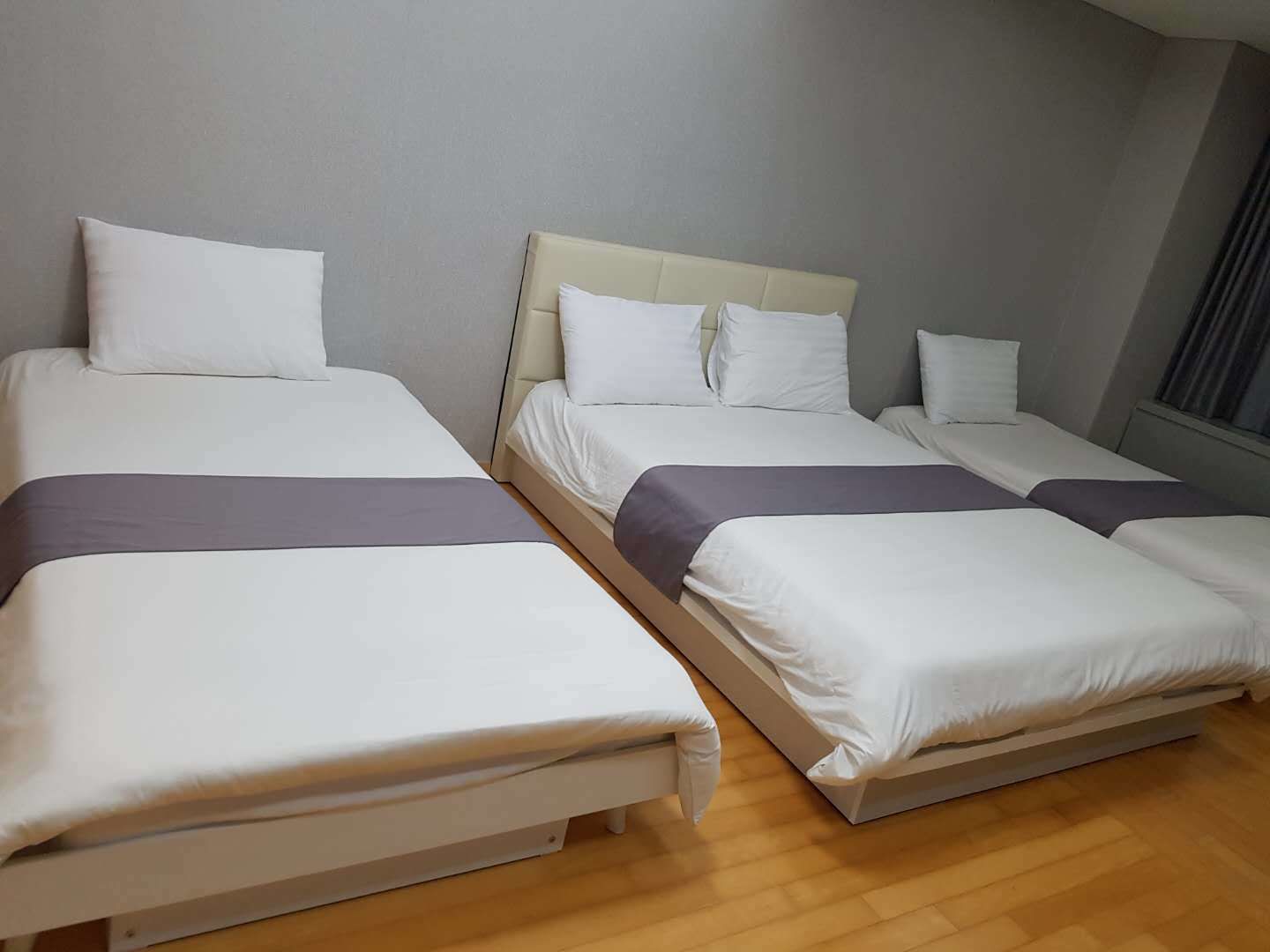 A hotel room with three single beds, each with white bedding and a grey accent.
